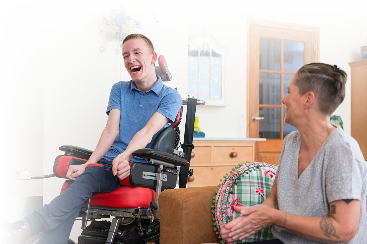Photo of a young man in a power wheelchair with a female friend as they laugh.
